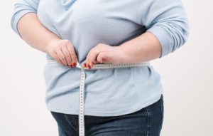 An overweight woman measuring her waistline.